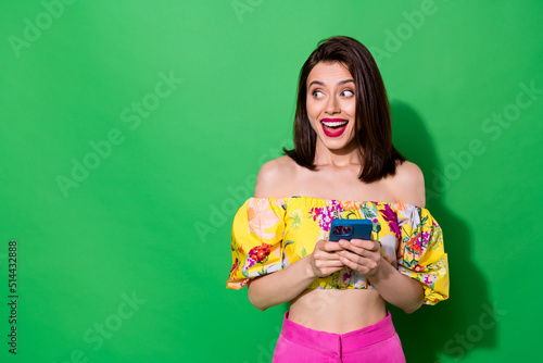 Photo of adorable excited lady wear off shoulders blouse looking empty space chatting modern gadget isolated green color background