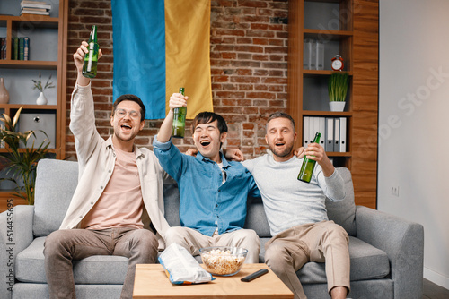 Three men watching a football game on tv and drinking a beer