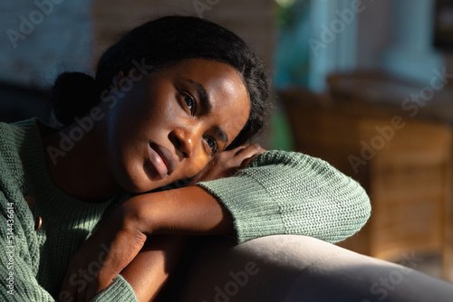 Lonely african american young woman looking away while resting head on sofa at home, copy space photo