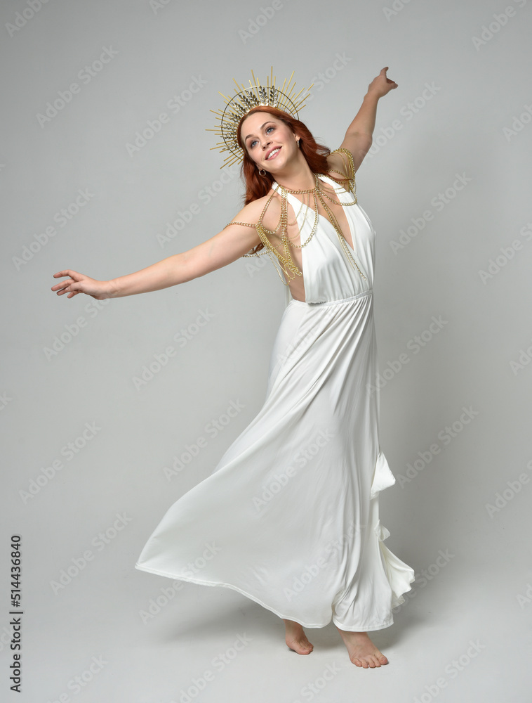 Full length portrait of beautiful red head woman wearing long flowing fantasy toga gown with golden halo crown jewellery, standing pose isolated on a white studio background.
Full length portrait of beautiful red head woman wearing long flowing fantasy toga gown with golden halo crown jewellery, standing pose isolated on a white studio background.