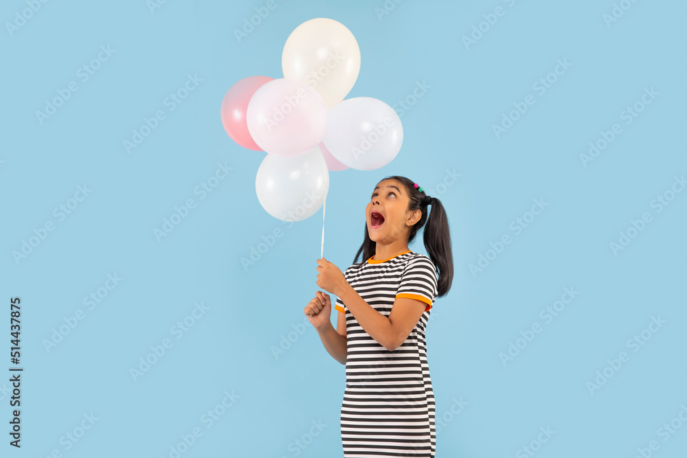 Excited girl holding colourful balloons against blue background Excited girl holding colourful balloons against blue background