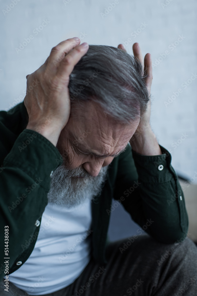 stressed senior man with beard touching head while suffering from headache at home. stressed senior man with beard touching head while suffering from headache at home.