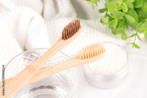 Bamboo toothbrushes with mineral toothpowder kaolin in alu container at white table against green leaves as background. Natural bath products, organic dentifrice