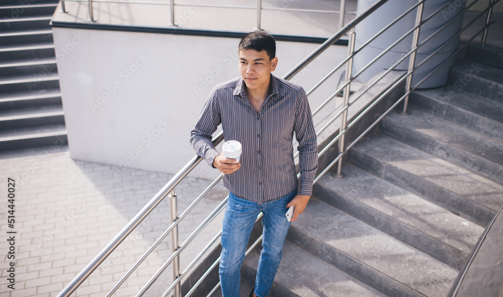 Asian guy with smartphone and coffee on stairs Asian guy with smartphone and coffee on stairs