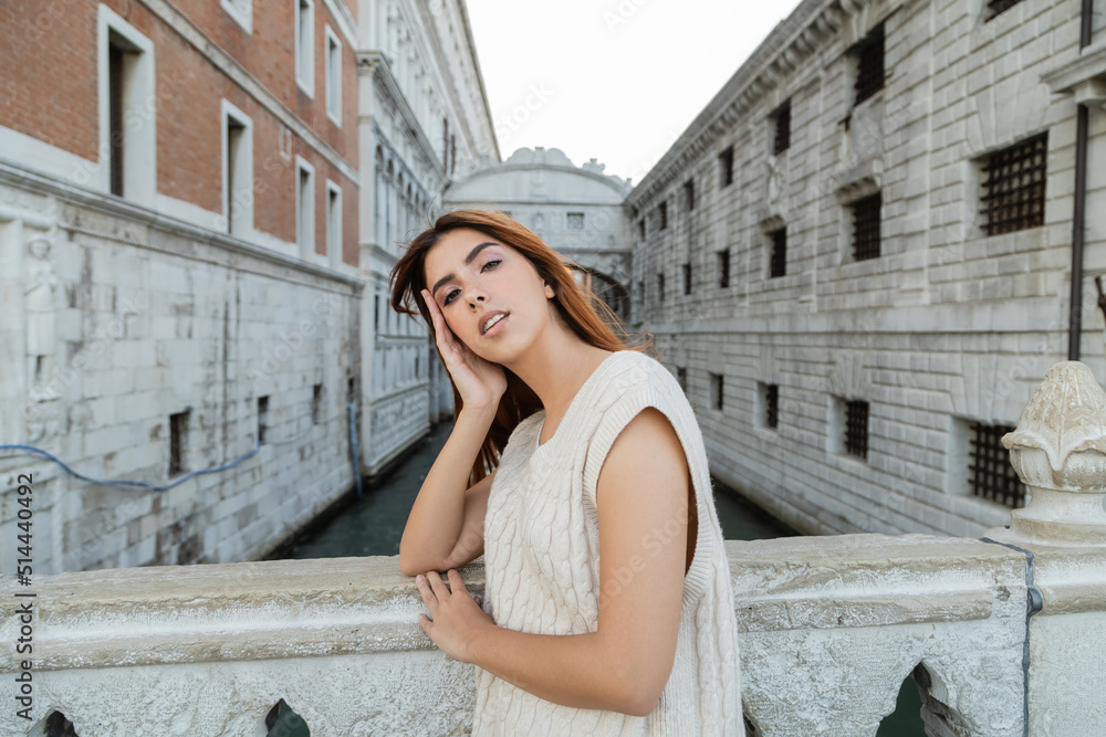 young woman with hand near fence looking at camera near medieval prison in Venice.
