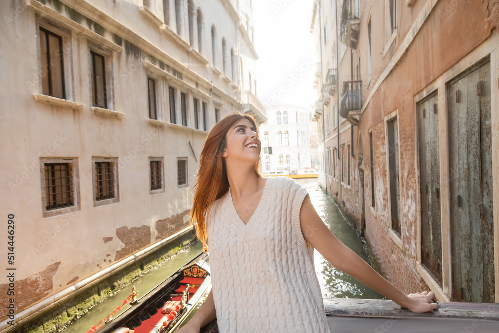happy redhead woman in summer knitwear looking at medieval buildings in Venice.