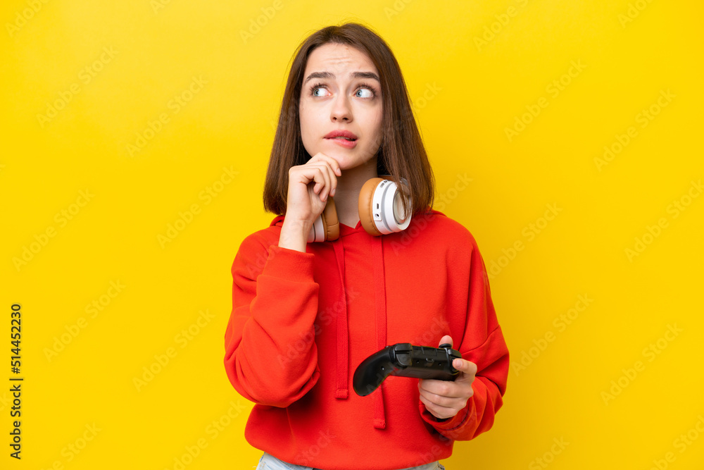 Young Ukrainian woman playing with a video game controller isolated on yellow background having doubts and thinking Young Ukrainian woman playing with a video game controller isolated on yellow background having doubts and thinking