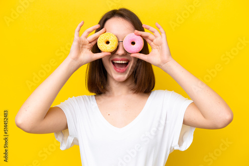 Young Ukrainian woman isolated on yellow background holding donuts in an eye