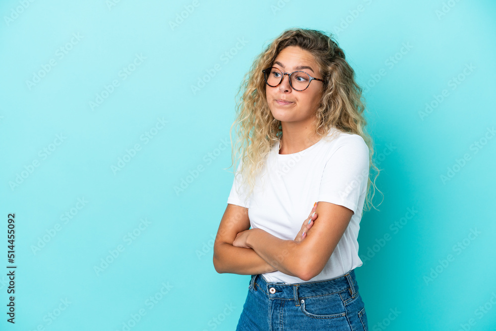 Girl with curly hair isolated on blue background making doubts gesture while lifting the shoulders Girl with curly hair isolated on blue background making doubts gesture while lifting the shoulders