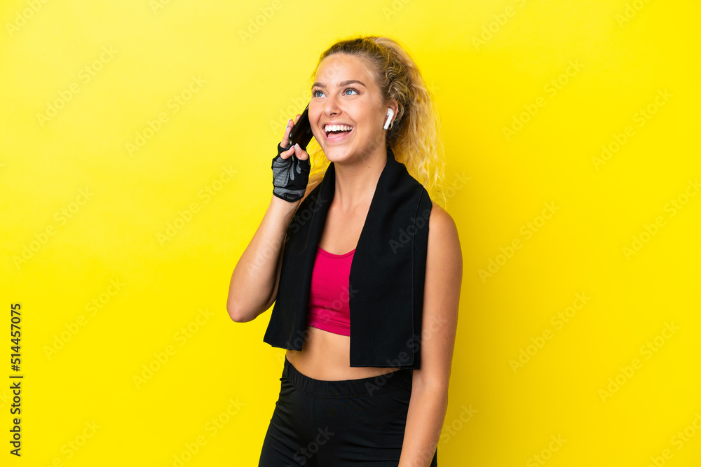 Sport woman with towel isolated on yellow background keeping a conversation with the mobile phone Sport woman with towel isolated on yellow background keeping a conversation with the mobile phone