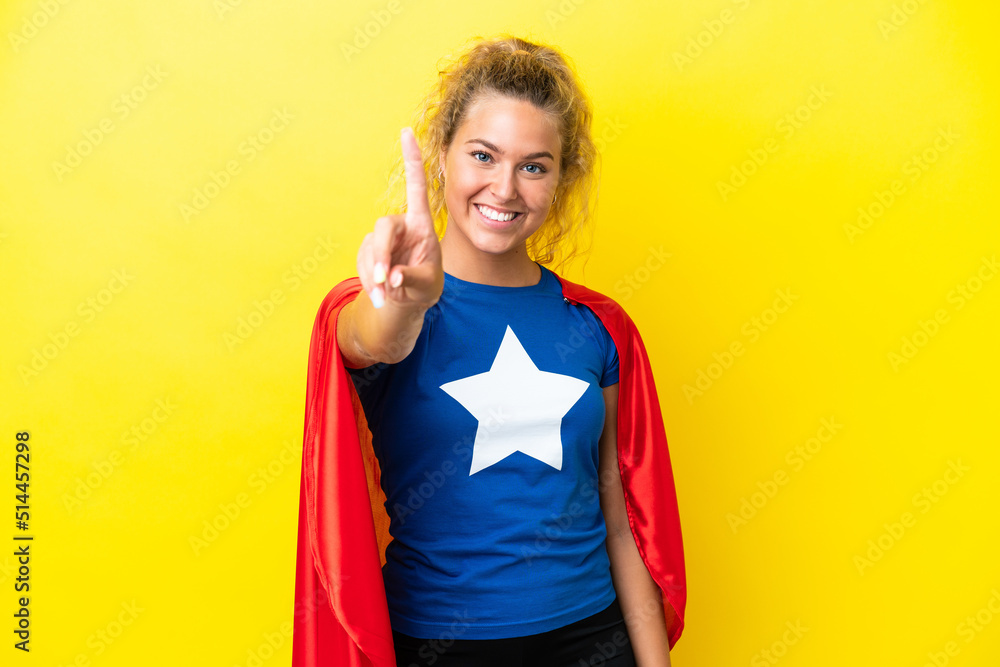 Girl with curly hair isolated on yellow background in superhero costume and pointing to the front Girl with curly hair isolated on yellow background in superhero costume and pointing to the front