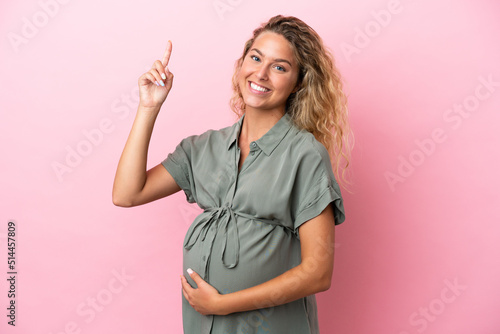 Girl with curly hair isolated on pink background pregnant and pointing up © luismolinero