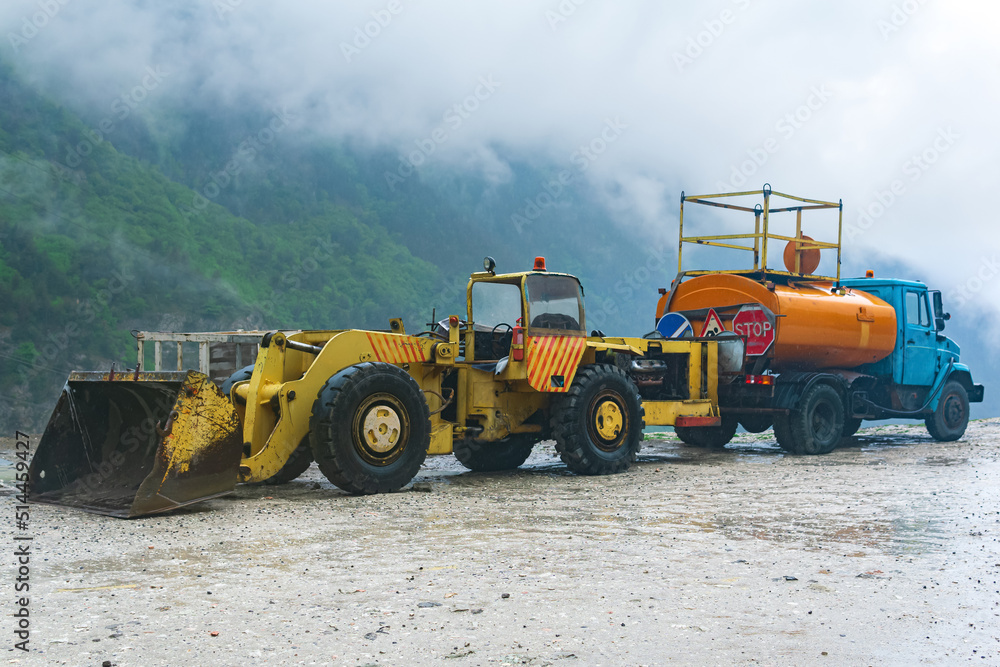 heavy road equipment for landslide raking stands by the roadside in a mountainous area during stormy weather