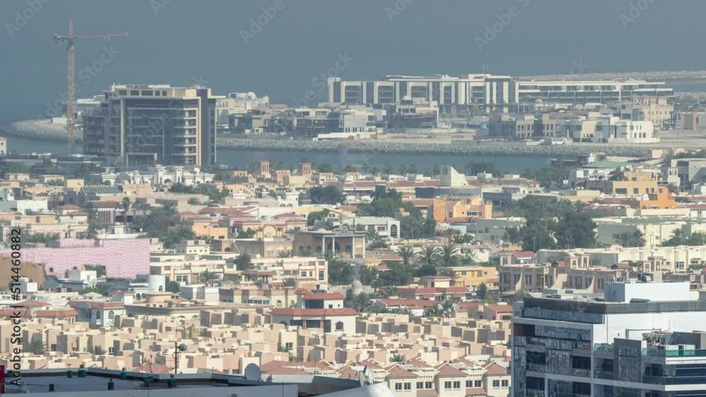 Aerial view of apartment houses and villas in Dubai city timelapse from skyscraper in financial district, United Arab Emirates. Island in the sea and building under construction