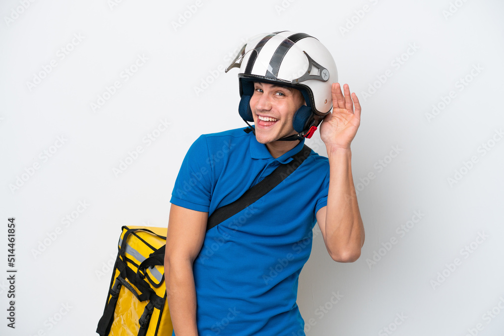 Young caucasian man with thermal backpack isolated on white background listening to something by putting hand on the ear