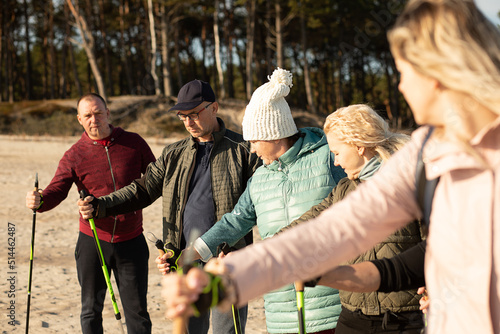 Leader woman and people group making Nordic walking with professional trekking sticks at the beach. Exercises education © Татьяна Волкова