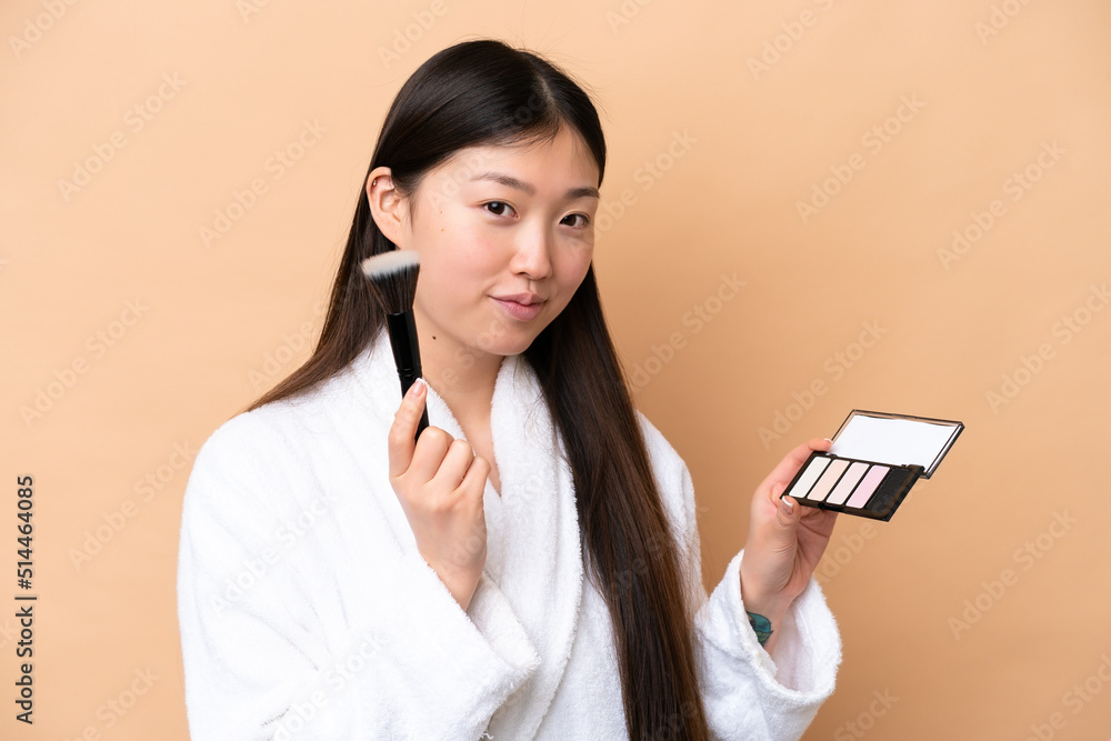 Young Chinese woman isolated on beige background with makeup palette Young Chinese woman isolated on beige background with makeup palette