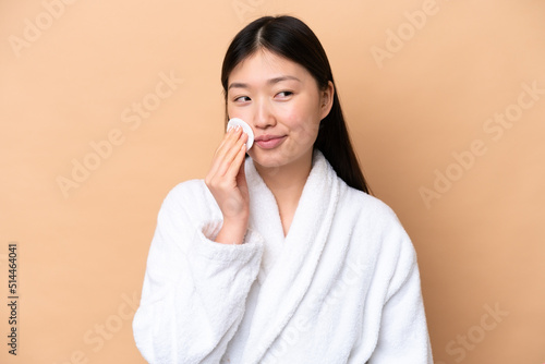 Young Chinese woman isolated on beige background with cotton pad for removing makeup from her face
