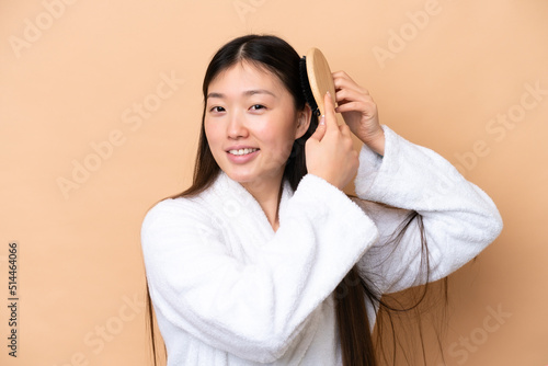 Young Chinese woman isolated on beige background with hair comb