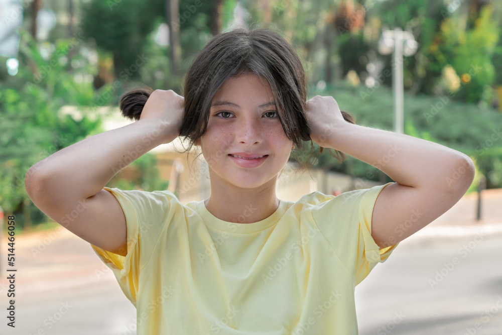 A young girl holds hair in her hands in a ponytail.
