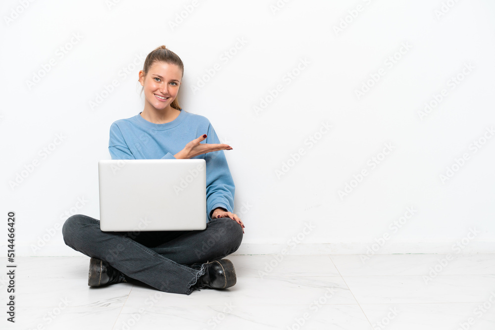 Young woman with a laptop sitting on the floor presenting an idea while looking smiling towards Young woman with a laptop sitting on the floor presenting an idea while looking smiling towards
