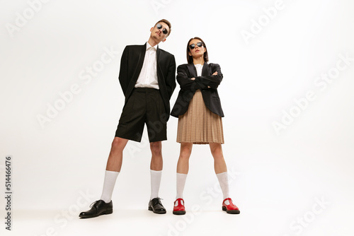 Full-length portrait of stylish young couple, man and woman in retro suit posing isolated over grey studio background