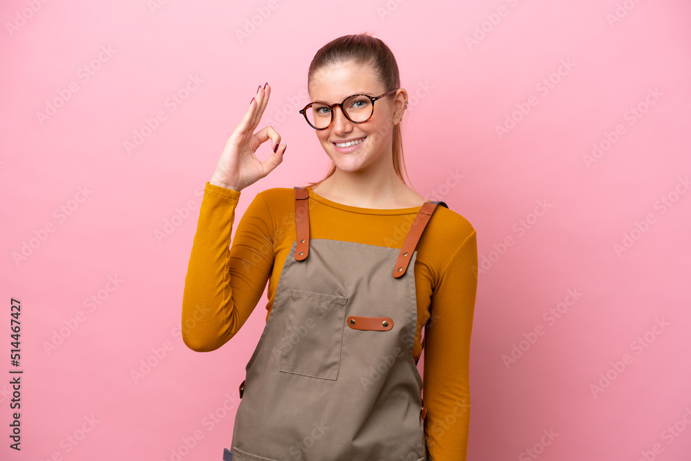 Woman with apron isolated on pink background showing ok sign with fingers Woman with apron isolated on pink background showing ok sign with fingers