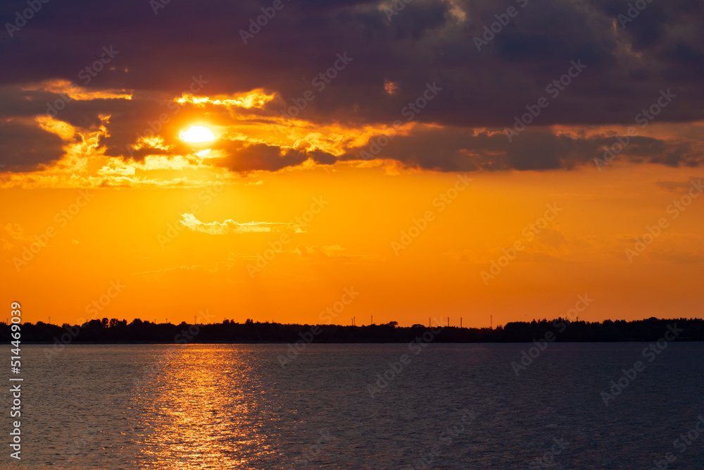 Beautiful colorful yellow orange blue sunset over the sea with sun reflections on the calm water surface and copy space on the clouds
