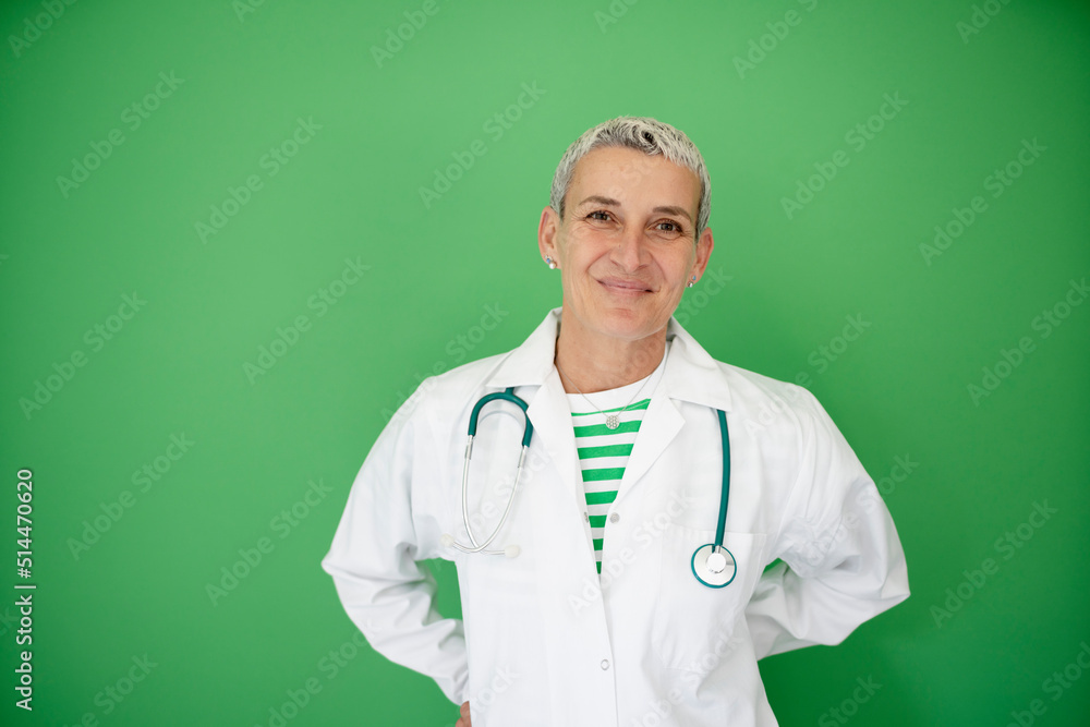 successful middle aged alternative woman doctor with short hair wearing white coat and stethoscope posing on green background successful middle aged alternative woman doctor with short hair wearing white coat and stethoscope posing on green background