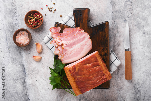 Whole Smoked Slab Bacon. Brisket. Sliced smoked gammon on a wooden table with rosemary, parsley, pepper, salt, and garlic on old gray concrete table background. Copy space.