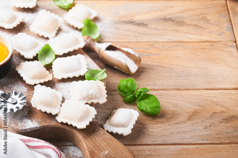 Ravioli Italian food. Tasty homemade pasta ravioli with flour, tomatoes, eggs and greens basil on wooden background. Process of making italian ravioli. Food cooking ingredients background. Top view.