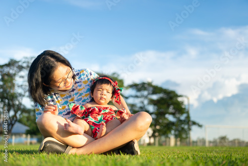 A lovely couple of mother and infant baby are enjoy playing at the outdoor park, with colorful blue sky as background. Family portrait photo.