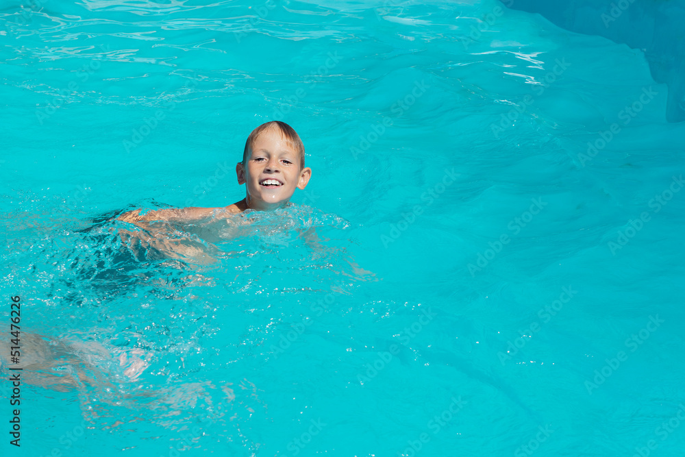 the boy swims in the azure water of the pool, basking in the sun
