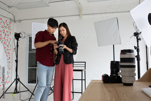 An Asian model is checking the photo on the camera, with an Asian photographer standing beside her. With both smiling faces and their finger point to the camera