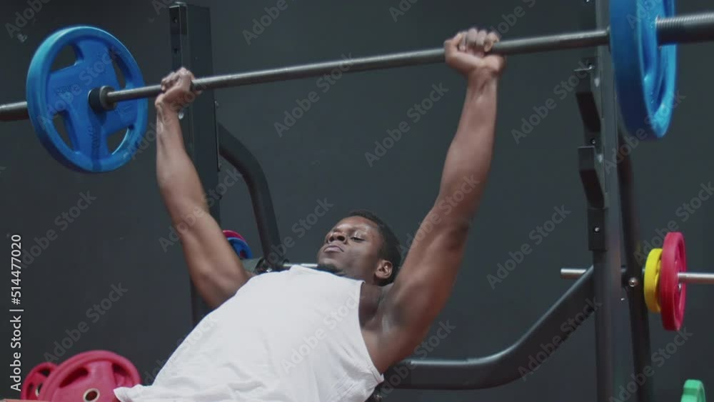 Young muscular afro powerful man does a bench press with a barbell lying on a bench.
