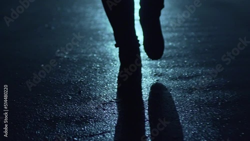 Legs of a man in backlight walking down the street at night.