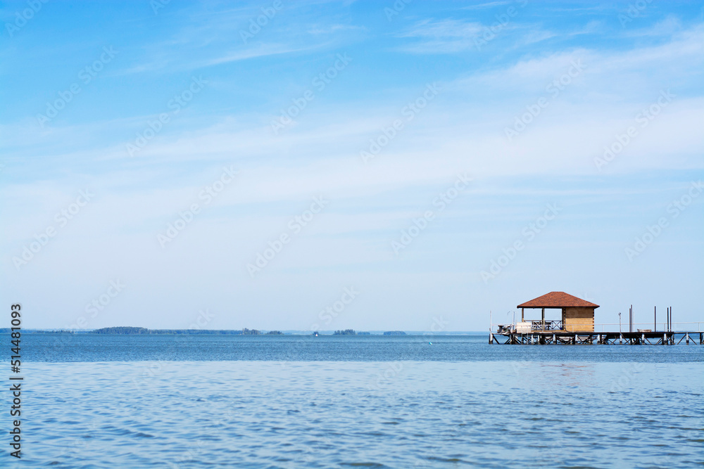 Sunny summer day with a cloudless blue sky, a wooden lonely house on the water of a lake or river, a horizontal photo without people