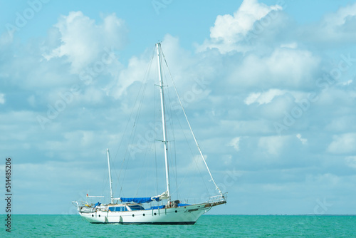 Single-deck white yacht on turquoise water. Sailboat with folded sail in the open sea in calm.