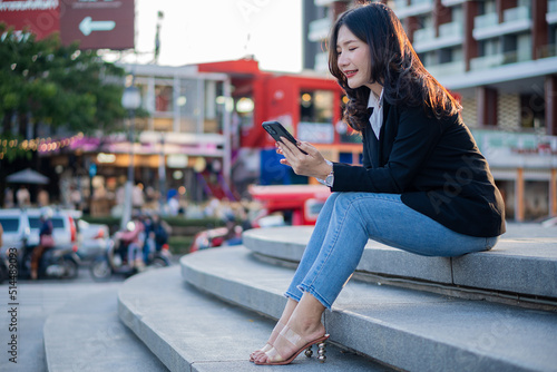 Asian businesswoman working outside on a smartphone looking at a screen in a business district. professional woman sitting outside