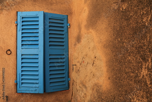 Blue shuttered window, partially open, set in a sandy coloured wall, copy space to side, Corsica, France