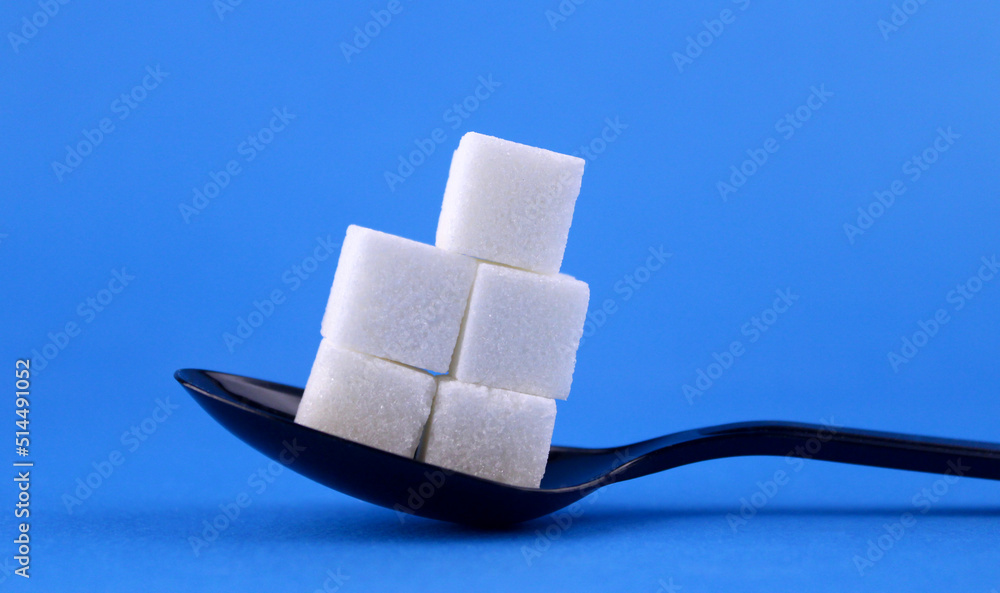 Obraz premium Sugar cubes in a black spoon on a blue background