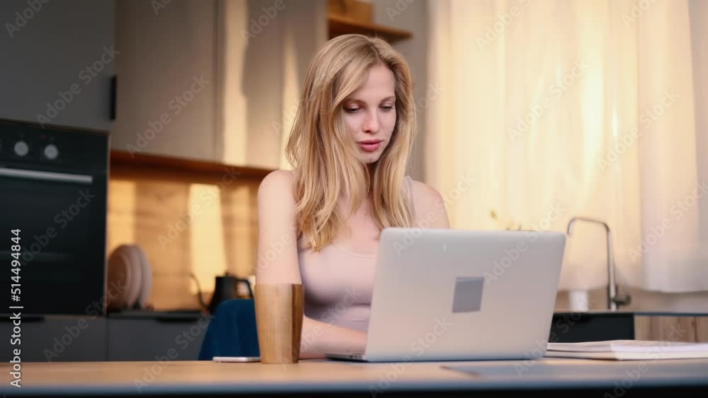 Portrait of attractive woman using laptop in modern domestic kitchen. Young woman sitting in front open laptop computer. Study, learning, remote work, freelance.