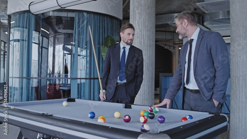 Photos Two businessmen playing billiards in office, active rest during break at work