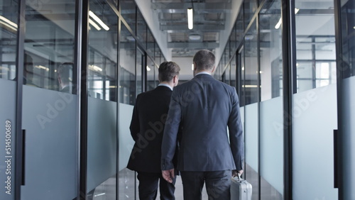 Two businessmen walking along office building corridor, business meeting with partners