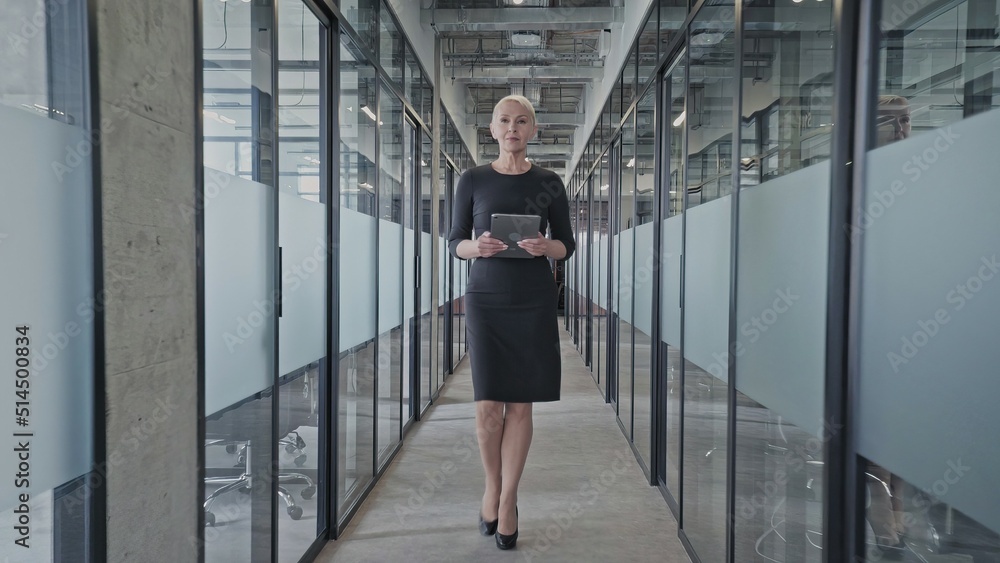 Successful businesswoman walking in company office corridor, tablet in hands Successful businesswoman walking in company office corridor, tablet in hands
