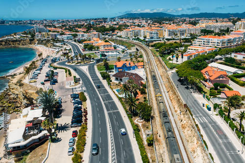 Aerial drone view of train passing near the Marginal Avenue and coastline with Parade district in Greater Lisbon, Portugal © Alexandre Rotenberg