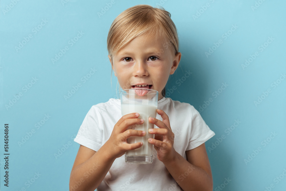Cute toddler caucasian girl smiling and drinking milk from the glass on the blue background. Benefits of milk and calcium for children Cute toddler caucasian girl smiling and drinking milk from the glass on the blue background. Benefits of milk and calcium for children