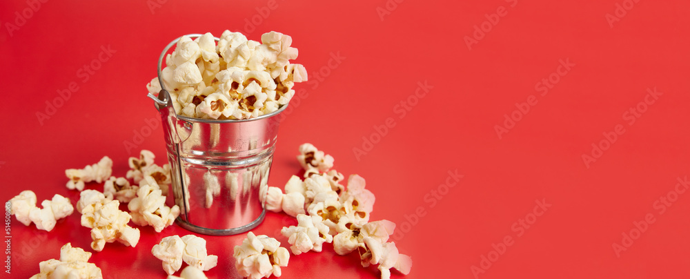 A small bucket filled with popcorn on a red background.