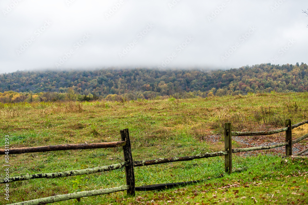 Virginia rural countryside farm cloudy mist fog day with wooden traditional fence by agricultural field in springtime or fall autumn with fallen dry brown leaves