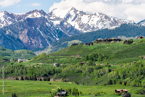 Mount Crested Butte town ski resort village mountain peak in summer with lodging houses on hills and green grass open valley and snowcapped rocky mountains photo
